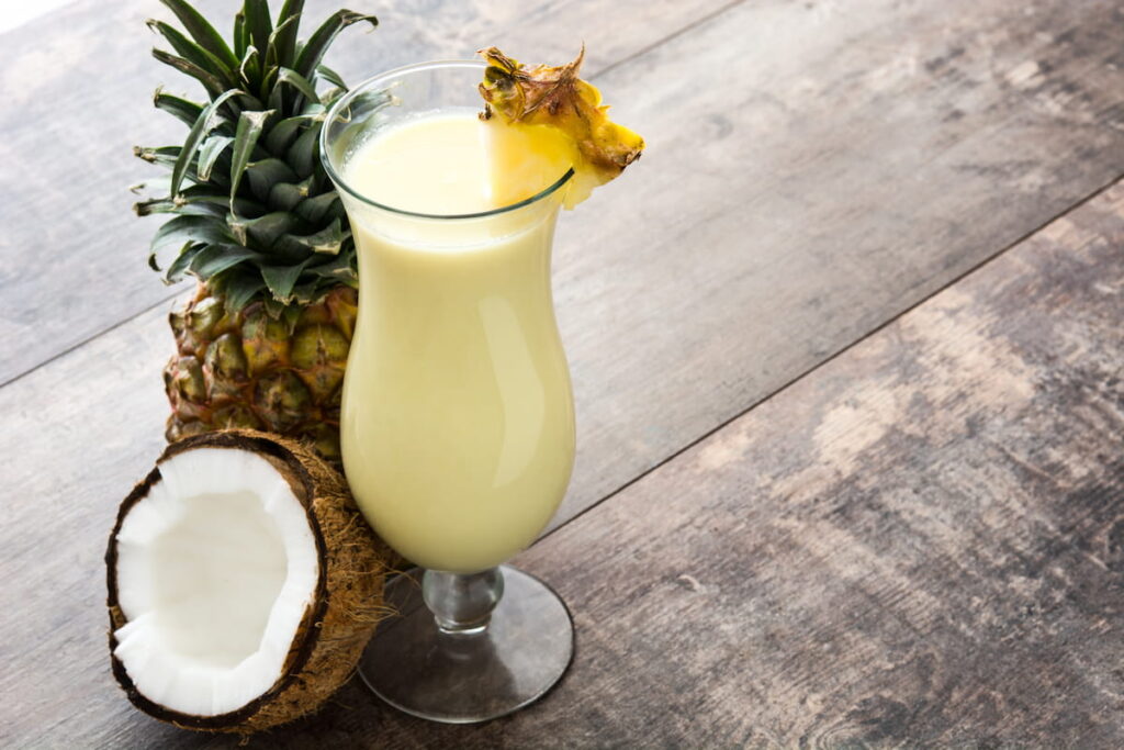 Pina colada drink in a hurricane glass on wood table, trending beverage flavors
