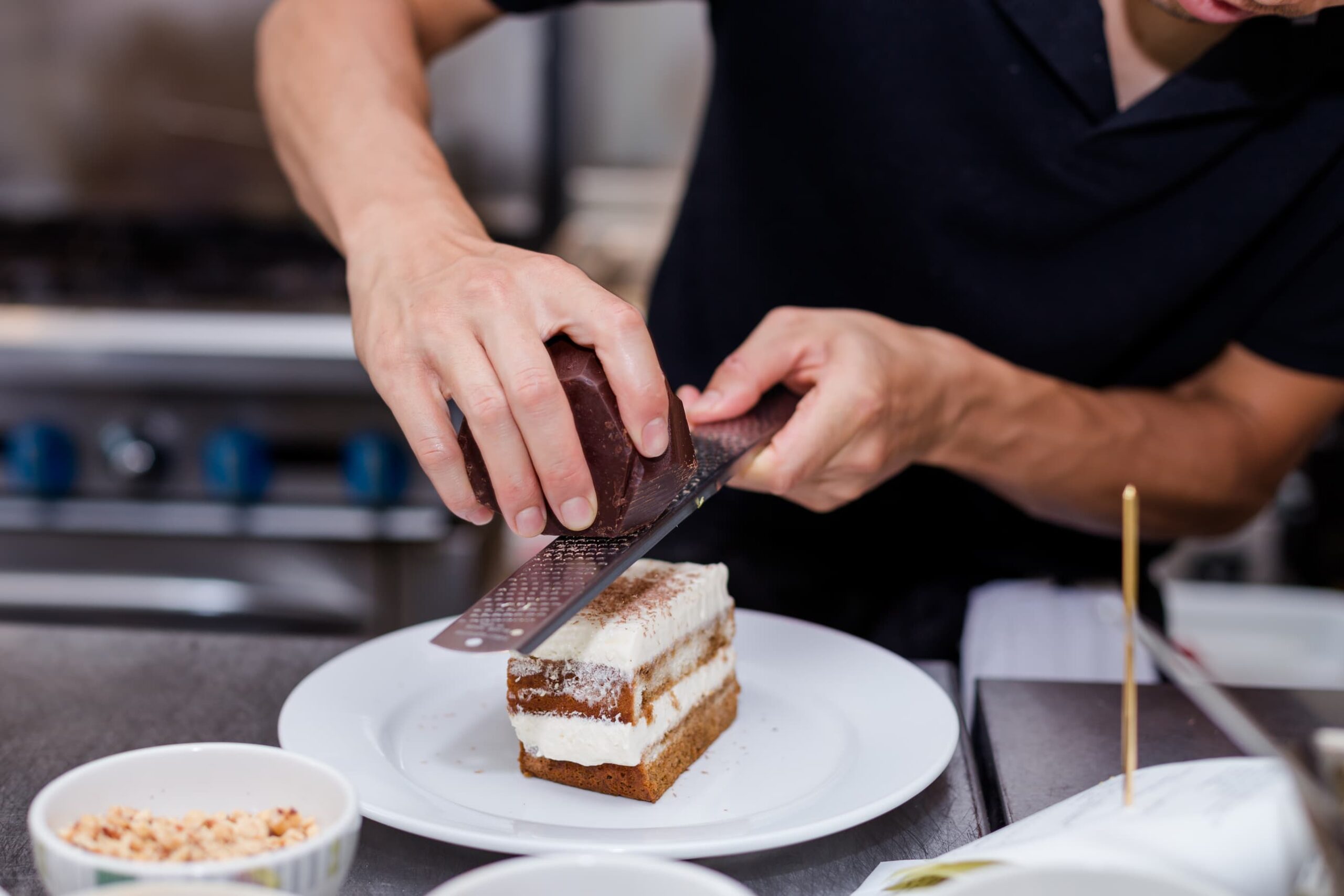 grating chocolate on top of a slice of tiramisu