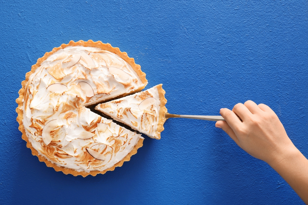 Fresh coconut pie with hand taking a slice, example of spring flavor trends