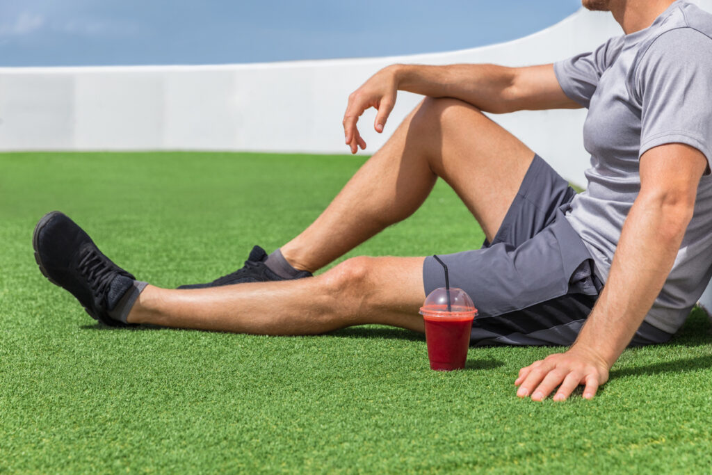 Juice Smoothie Sport Man Relaxing Enjoying Post Workout Morning Breakfast Sitting On Outdoor Grass At Home Or Fitness Gym. Athlete Drinking Red Fruit Smoothie Drink