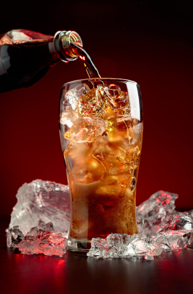 Sparkling Cola Is Poured From A Bottle Into A Misted Glass With Ice.