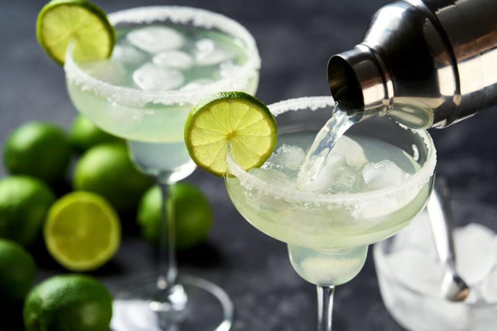 Margarita Cocktail Is Poured From A Shaker Into A Glasses And Lime And Salt Rim , Selective Focus.